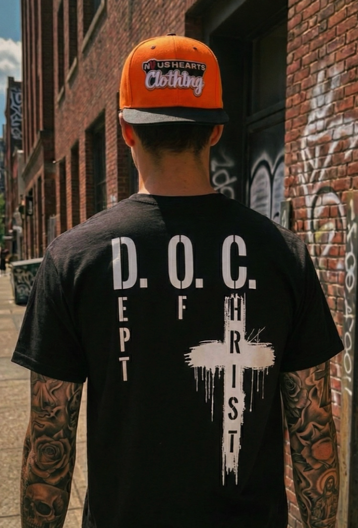 Man in an alley wearing the black Dept of Christ t-shirt and an orange cap, back print facing camera