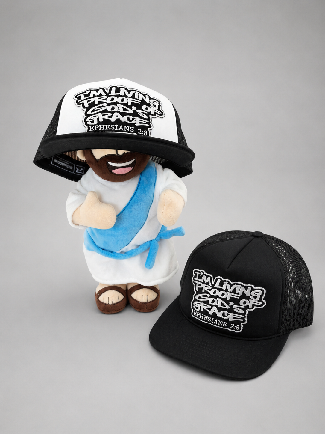 Plush figure wearing the white Living Proof trucker hat, black hat beside it